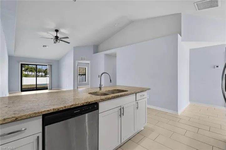 Kitchen with lofted ceiling, dishwasher, light stone countertops, white cabinetry, and a ceiling fan