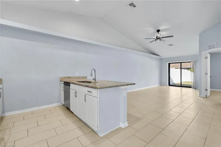Kitchen with a peninsula, white cabinets, lofted ceiling, open floor plan, and light stone counters