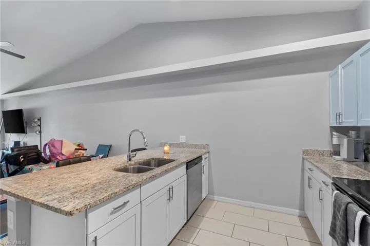 Kitchen featuring a peninsula, light stone counters, lofted ceiling, and white cabinetry