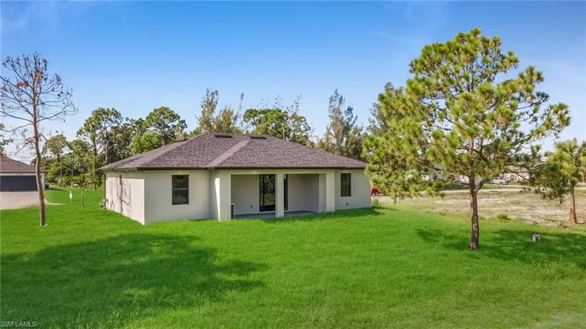Rear view of property with a lawn, a patio, stucco siding, and roof with shingles