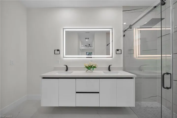 Full bathroom featuring a marble finish shower, light marble finish flooring, and double vanity