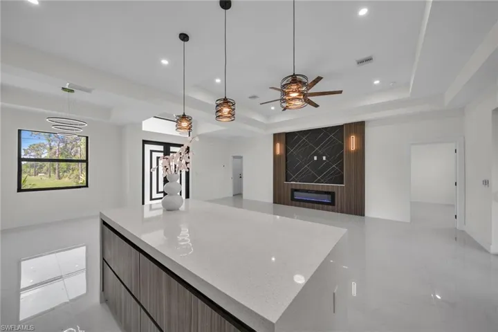 Kitchen with open floor plan, a tray ceiling, modern cabinets, light stone counters, and a large fireplace