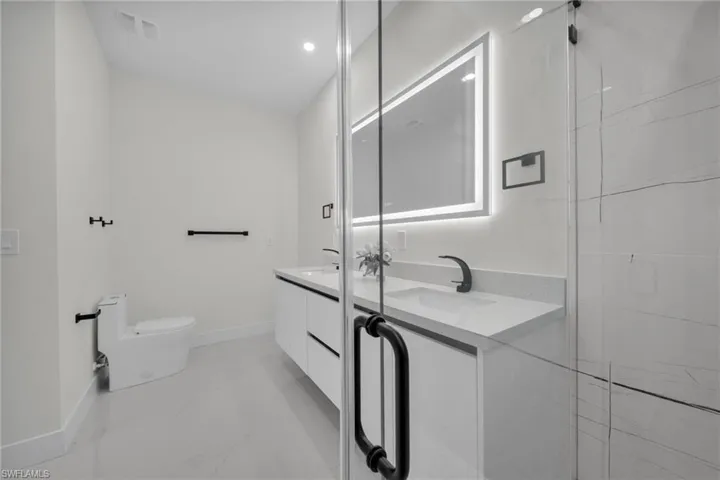 Bathroom featuring double vanity, light marble finish floors, and recessed lighting