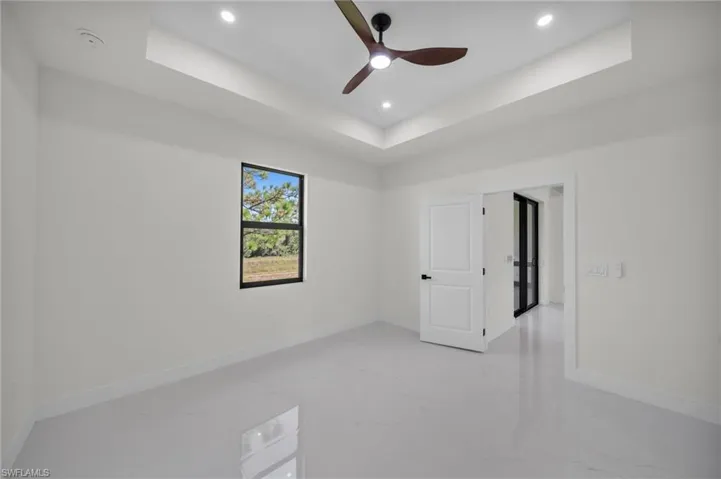 Unfurnished room with a raised ceiling, light marble finish floors, a ceiling fan, and recessed lighting