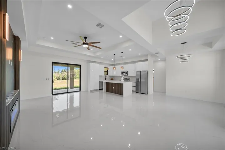 Unfurnished living room featuring a raised ceiling, recessed lighting, a ceiling fan, and light marble finish floors