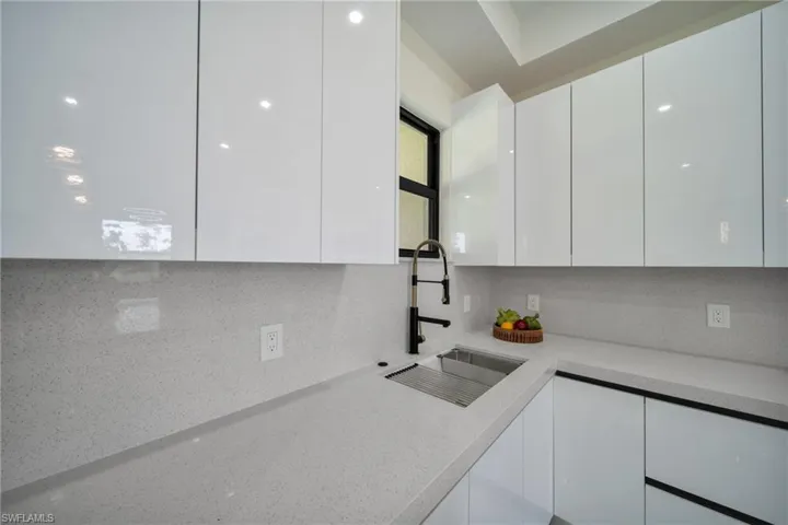 Kitchen with white cabinets, modern cabinets, light stone countertops, and decorative backsplash