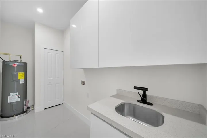 Laundry room featuring washer hookup, water heater, light marble finish floors, cabinet space, and recessed lighting