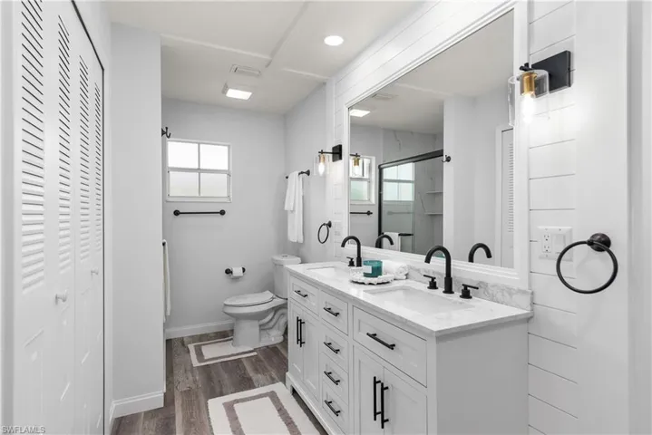 Bathroom with a closet, double vanity, a shower stall, and dark wood-type flooring