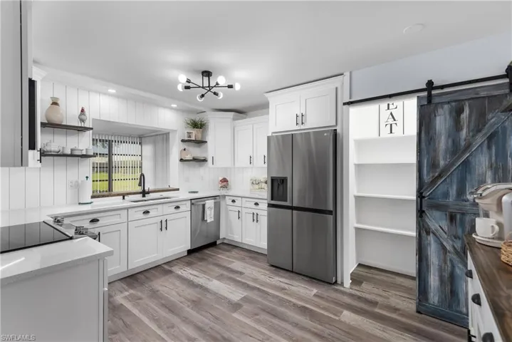 Kitchen featuring open shelves, stainless steel appliances, white cabinetry, light stone counters, and a barn door