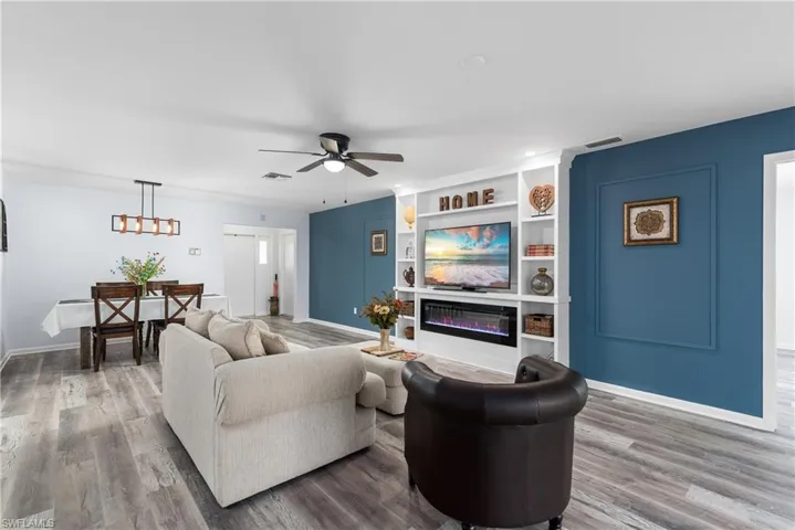 Living room with built in features, a glass covered fireplace, wood finished floors, and a ceiling fan