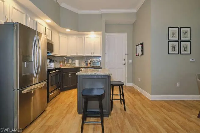 Kitchen with dual tone cabinetry, stainless steel appliances, crown molding, a breakfast bar area, and light wood-style floors