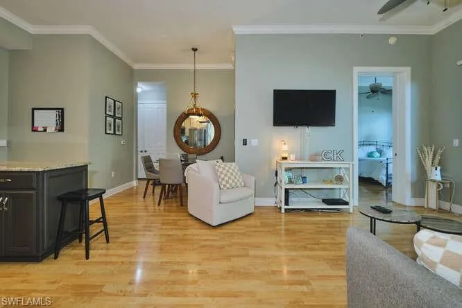 Living room with light wood finished floors, ornamental molding, and ceiling fan