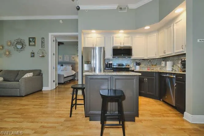 Kitchen featuring two tone color scheme, crown molding, stainless steel appliances, light stone countertops, and a kitchen bar