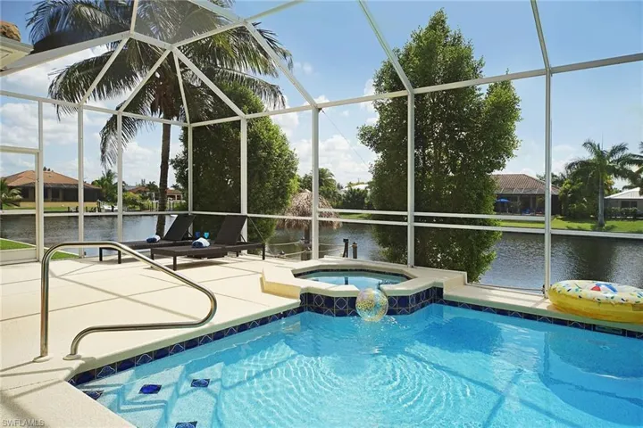 Swimming pool featuring a patio area, a water view, an in-ground hot tub, and glass enclosure