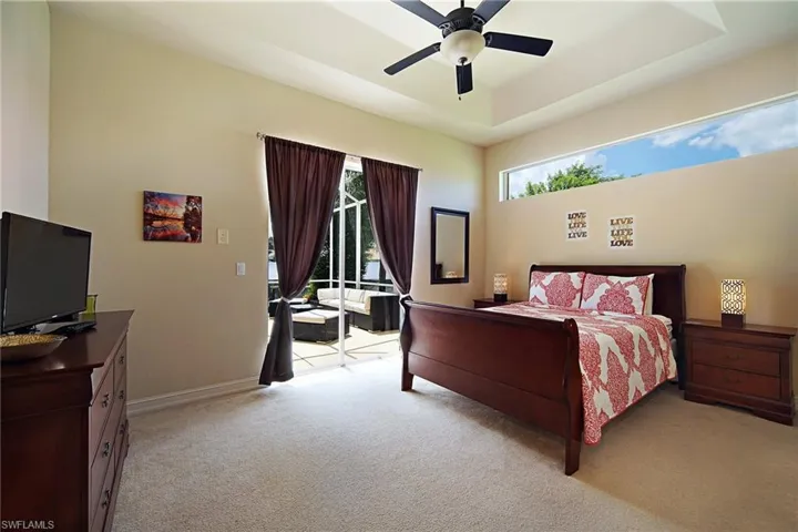 Bedroom featuring access to exterior, light carpet, baseboards, a ceiling fan, and a tray ceiling