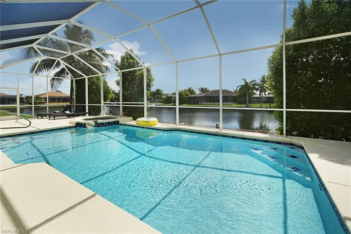 View of pool with a patio area, a water view, a pool with connected hot tub, and glass enclosure