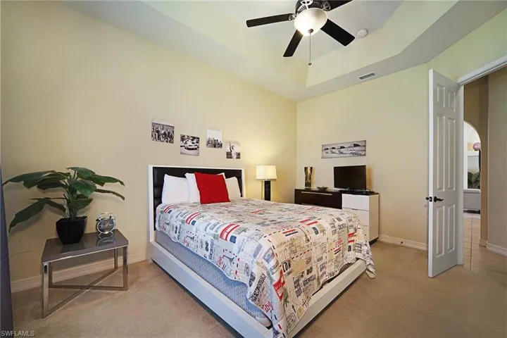 Bedroom featuring carpet floors, a raised ceiling, baseboards, and ceiling fan