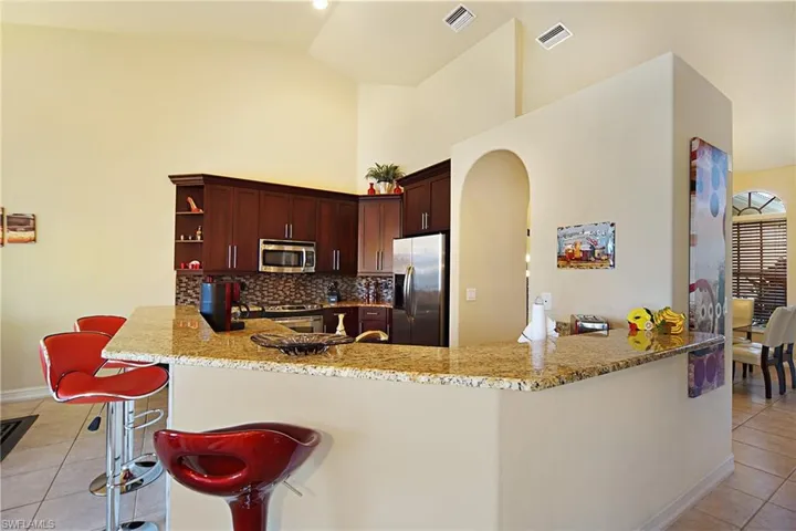 Kitchen with appliances with stainless steel finishes, light tile patterned floors, arched walkways, high vaulted ceiling, and light stone countertops