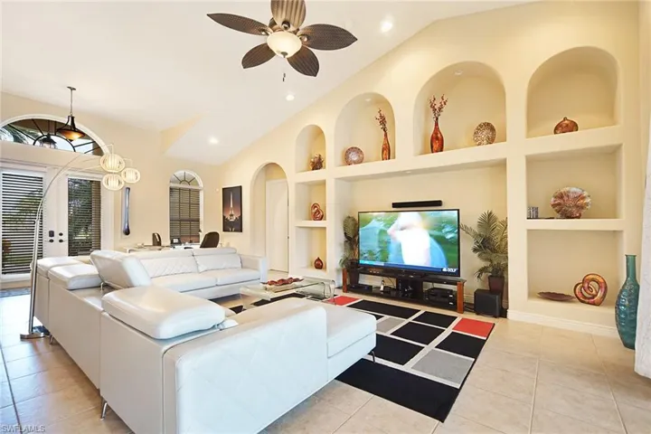 Living area featuring built in shelves, vaulted ceiling, ceiling fan, arched walkways, and light tile patterned floors