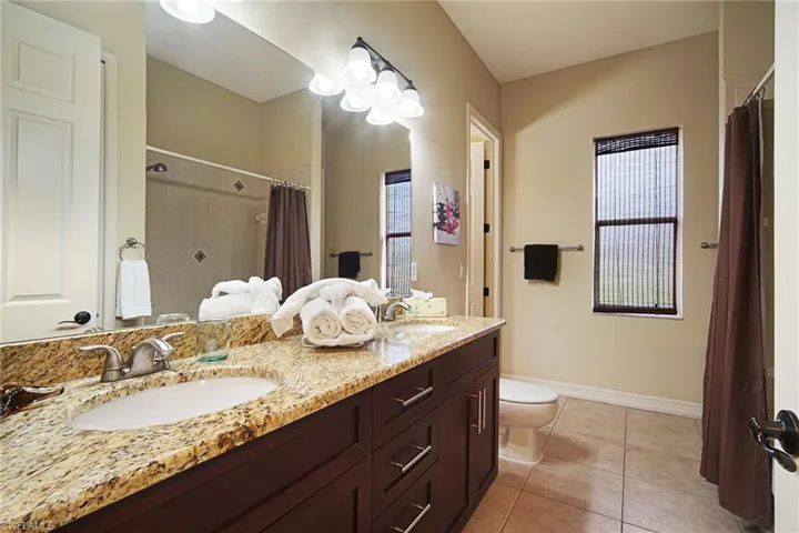 Bathroom with toilet, baseboards, tile patterned flooring, double vanity, and a shower with curtain