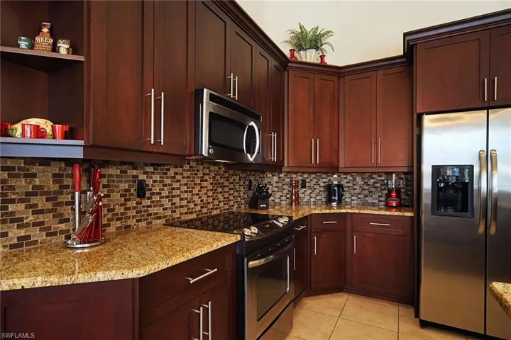 Kitchen with appliances with stainless steel finishes, light tile patterned floors, light stone countertops, decorative backsplash, and open shelves