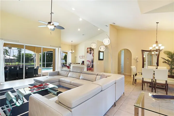 Living area with a chandelier, ceiling fan, high vaulted ceiling, arched walkways, and light tile patterned flooring