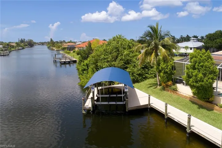 Dock featuring boat lift, a water view, a lanai, and a yard