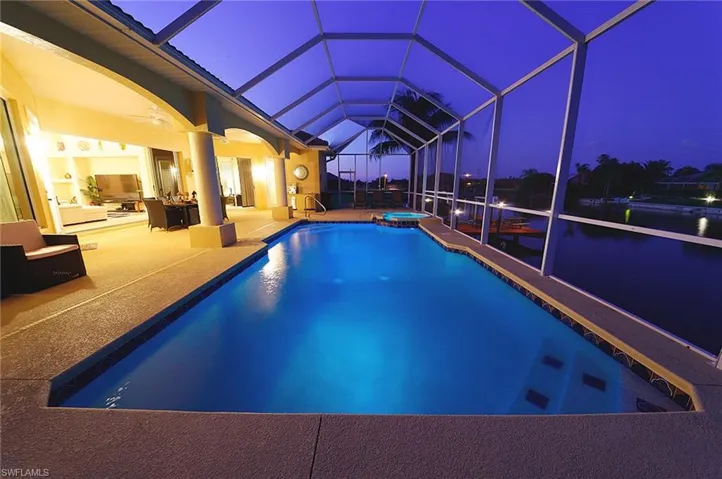 Pool at twilight with a patio, a pool with connected hot tub, and glass enclosure