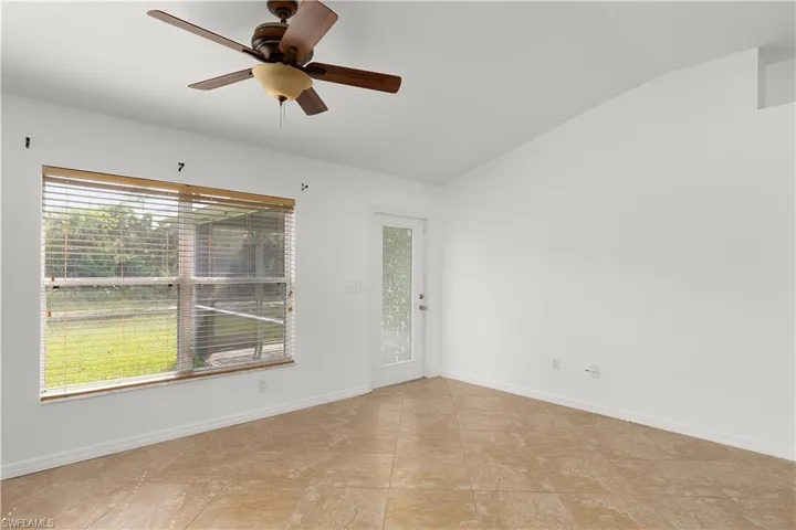 Tiled empty room featuring vaulted ceiling, a healthy amount of sunlight, and ceiling fan