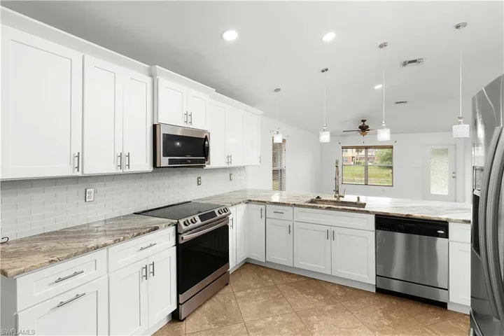 Kitchen with appliances with stainless steel finishes, sink, kitchen peninsula, decorative light fixtures, and white cabinets