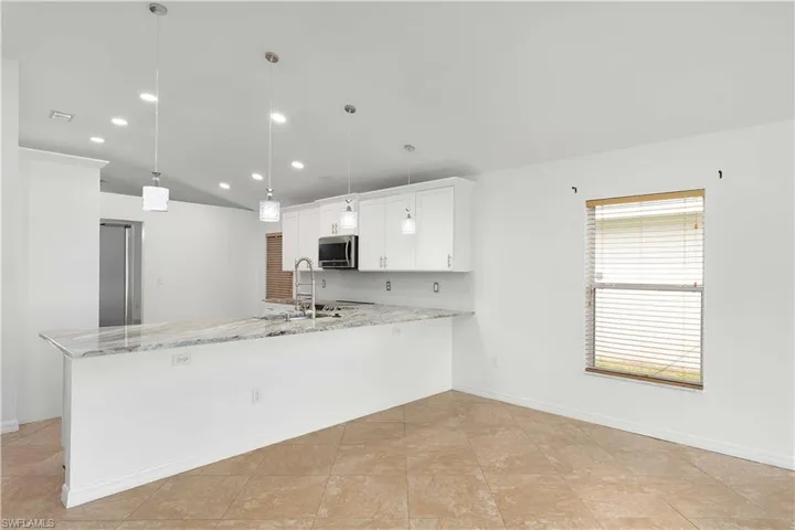 Kitchen featuring decorative backsplash, white cabinetry, light stone countertops, pendant lighting, and sink
