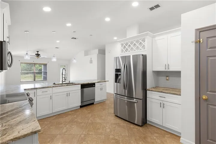 Kitchen featuring sink, stainless steel appliances, decorative light fixtures, white cabinets, and light stone counters