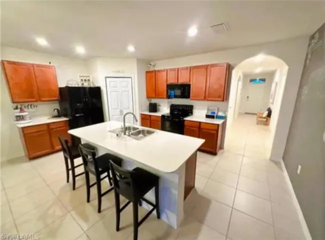Kitchen with light countertops, black appliances, arched walkways, a breakfast bar, and light tile patterned floors