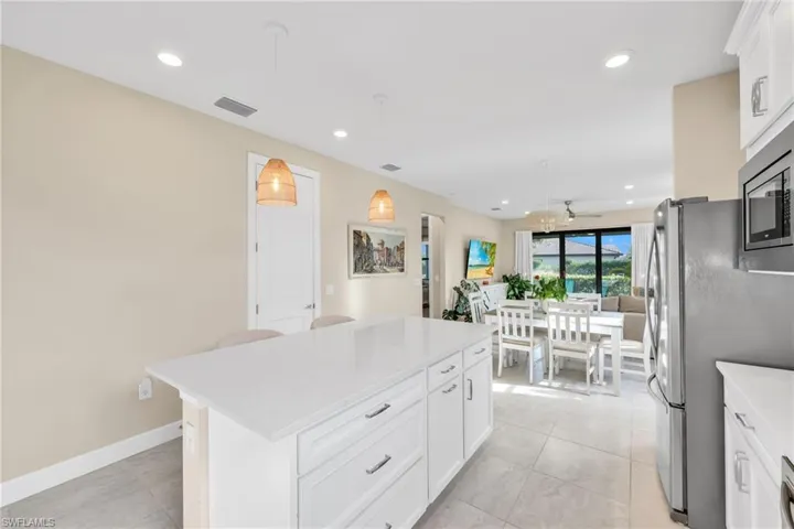 Kitchen with white cabinets, decorative light fixtures, a kitchen island, recessed lighting, and light stone countertops