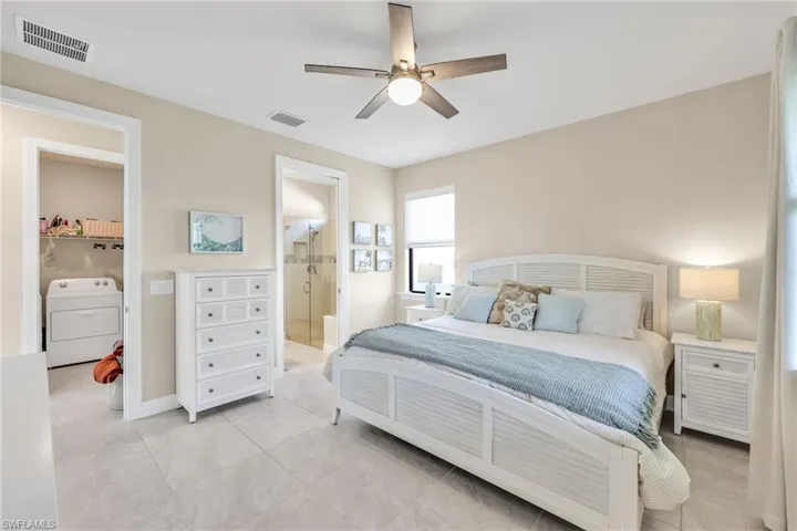 Bedroom featuring washer / clothes dryer, light tile patterned floors, a ceiling fan, and ensuite bath