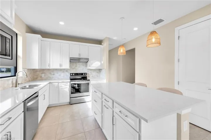 Kitchen with hanging light fixtures, tasteful backsplash, appliances with stainless steel finishes, white cabinetry, and a kitchen island