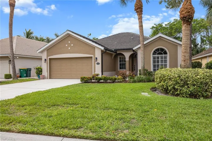 Stucco exterior with a tiled roof, arched window, attached garage, and mature palm trees