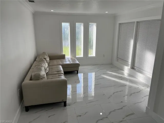 Living area with light marble finish floors, ornamental molding, and recessed lighting