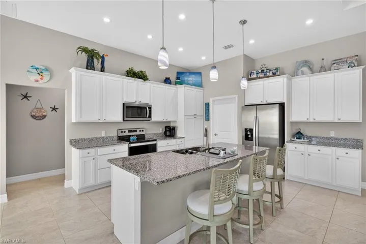 Kitchen with stainless steel appliances, a breakfast bar, white cabinetry, light stone counters, and an island with sink