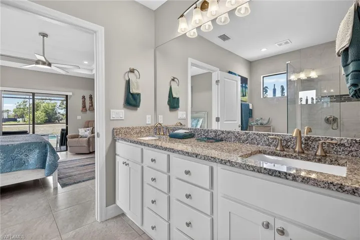 Ensuite bathroom with double vanity, a stall shower, a ceiling fan, light tile  floors, and recessed lighting