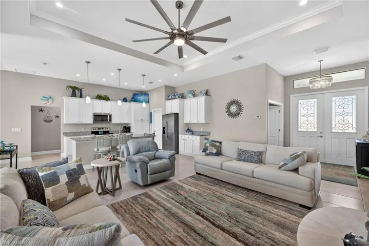 Living area with ceiling fan, ornamental molding, light tile floors, a high tray ceiling, and a huge designer fan