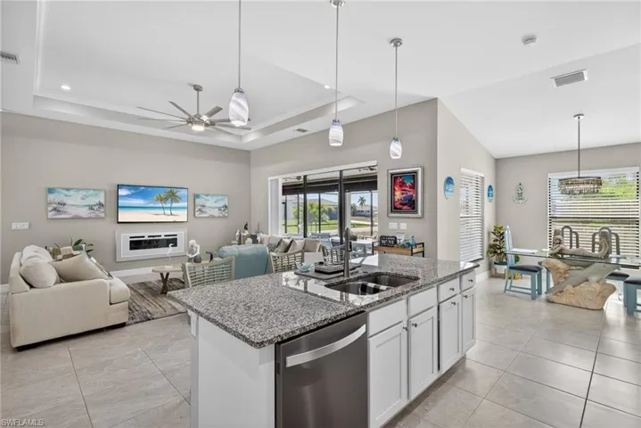 Kitchen with open floor plan, light stone countertops, hanging light fixtures, dishwasher, and an island with sink
