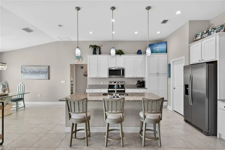 Kitchen with stainless steel appliances, hanging light fixtures, a center island with sink, white cabinetry, and light stone counters