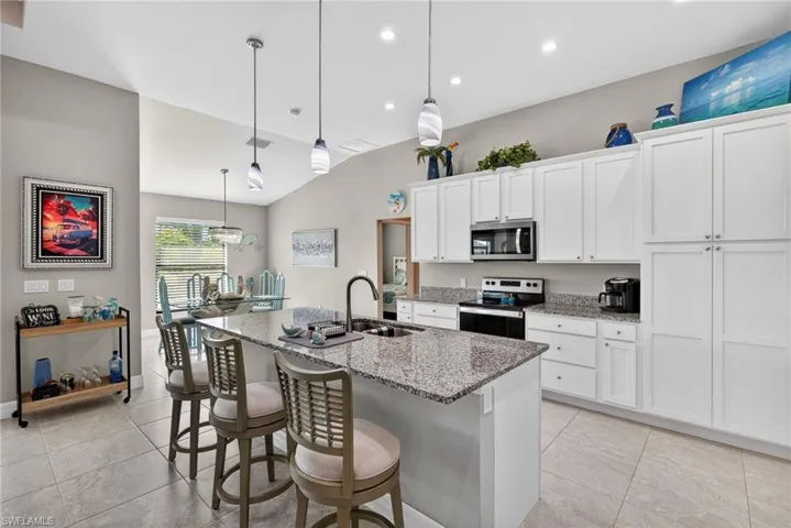 Kitchen with a breakfast bar area, stainless steel appliances, white cabinetry, light stone countertops, and a kitchen island with sink