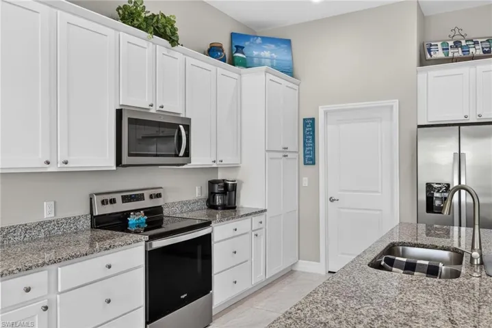 Kitchen featuring stainless steel appliances, light stone countertops, and white cabinetry