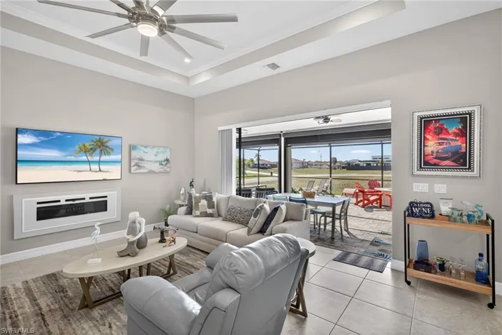 Living area with ceiling fan, ornamental molding, a raised ceiling, and light tile floors