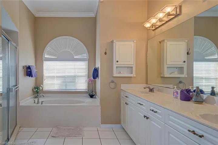 Bathroom featuring a bath, crown molding, double vanity, a sink, and a stall shower