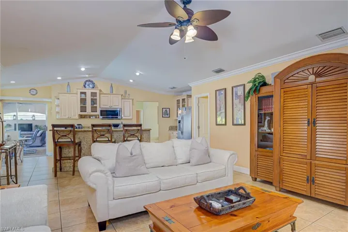 Living area featuring vaulted ceiling, light tile patterned floors, visible vents, ceiling fan, and ornamental molding