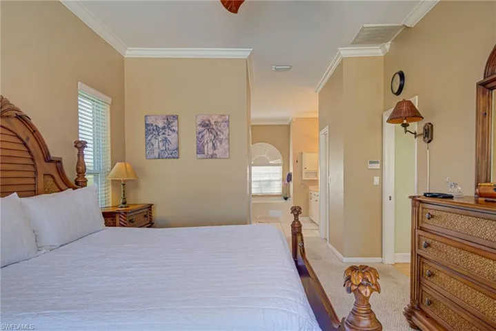 Bedroom featuring baseboards, ornamental molding, multiple windows, and light colored carpet