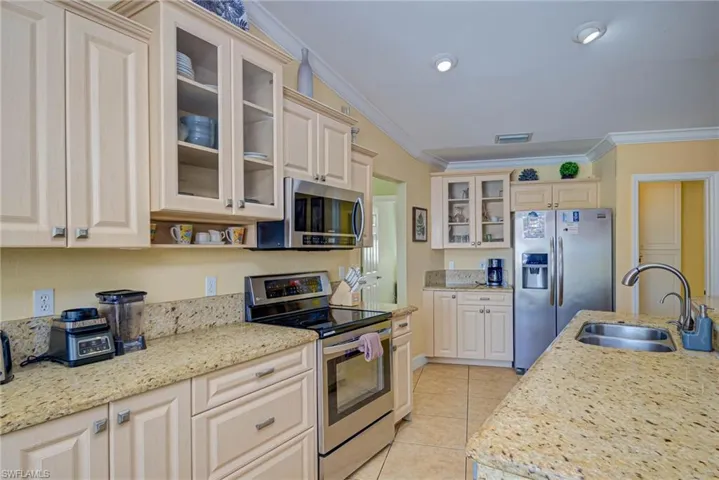 Kitchen featuring light tile patterned flooring, crown molding, appliances with stainless steel finishes, glass insert cabinets, and a sink